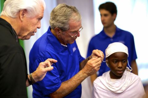 Former President George W. Bush fits a patient with hearing aids at a mission in Dar es Salaam, as Bill Austin, founder of the Starkey Hearing Foundation, looks on. (Photo: Starkey Hearing Foundation)