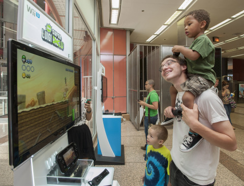In this photo provided by Nintendo of America, Jonathan K. with his little brother Quentin C. on his shoulders enjoys playing New Super Luigi U at the Clark/Lake 'L' Station in Chicago on Aug. 12, 2013. A Chicago 'L' train's interior and exterior are wrapped with a Luigi theme through Sept. 8 in celebration of the Year of Luigi and New Super Luigi U, which launches as a packaged game for Wii U on Aug. 25, 2013. (Photo by Peter Barreras/Invision for Nintendo/AP Images)