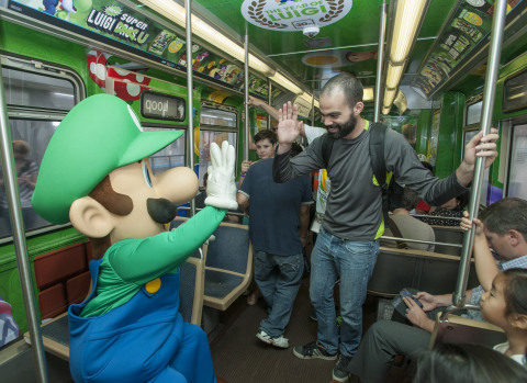 In this photo provided by Nintendo of America, Luigi high fives Gustavo M. of Caracas, Venezuela on board the Luigi-themed Chicago 'L' train, at the Clark/Lake Station in Chicago on Aug. 12, 2013. The train's interior and exterior are wrapped now through Sept. 8 in celebration of the Year of Luigi and New Super Luigi U, which launches as a packaged game for Wii U on Aug. 25, 2013. (Photo by Peter Barreras/Invision for Nintendo/AP Images)