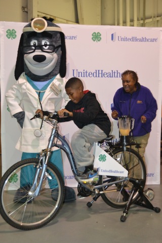 Cheered on by Dr. Health E. Hound and Mississippi 4-H program leader Manola Erby, nine year old Joseph Walker pedals to create a healthy smoothie using a "bike blender." The Family Fun and Fitness event was part of the UnitedHealthcare Mississippi 4-H "Eat4-Health" partnership, which aims to reduce obesity rates among young people and families through youth and community-based education and awareness programs. The activities at the Family Fun & Fitness Day are part of a series of trainings and events made possible by a $30,000 grant provided by UnitedHealthcare to Alcorn State University Extension Program, which administers 4-H programs to all counties in the state. (Photo: Business Wire)