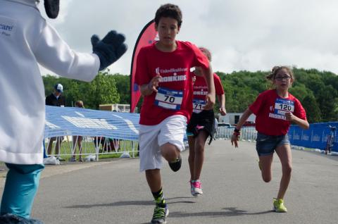 Boys & Girls Club of Lawrence youth Joaó Carlos Rameriz, Mia Ramirez and Biana Nieto (#120), all aged 10, are cheered on by UnitedHealthcare mascot Dr. Health E. Hound as they cross the finish line at the UnitedHealthcare IRONKIDS Kansas Fun Run at Clinton State Park. More than 150 youth participated in the race, including many from the Boys & Girls Club of Lawrence. UnitedHealthcare sponsored the race and made a $3,000 donation to the organization in support of youth healthy living programs and provided free race entries. Source: Kelly Prier.