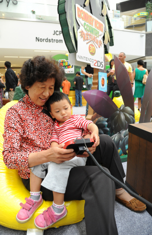 In this photo provided by Nintendo of America and released June 7, 2014, Ronghua W., 64, of China and her granddaughter Sophia X., 2, of Los Angeles, enjoy playing "Donkey Kong Country Returns 3D" at the Westfield Culver City mall on June 6, 2014. The free three-month "Play Nintendo Tour 2014" kicked off in Los Angeles on June 6 and will visit malls and events in a dozen major cities across the United States, showcasing games that feature kid-friendly characters like Donkey Kong, Mario and Kirby, all played on Nintendo 2DS, the latest member of Nintendo's hand-held family. (Photo by Nintendo/Bob Riha, Jr.)