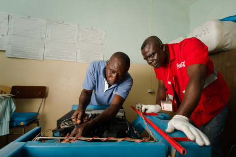 Coca-Cola Lead Cooler Technician, Maxwell Ayisi (right), and Ghana Health Service Refrigeration Technician, Livingstone Modey (left), repairing a dual gas/electric cooler used to store vaccines at a clinic in Peki Dzake in the Volta Region of Ghana. (Photo: Business Wire)