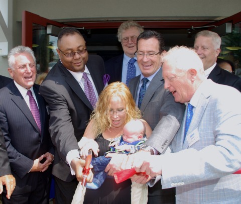 Robin DePaiva (center) and her newborn baby Patrick join Gov. Dannel Malloy and other dignitaries to help cut the ribbon marking the opening of Gini's House, a new, permanent supportive-housing community for women and their families in Norwalk. L to R: Norwalk Mayor Harry Rilling; Alan Mathis, President & CEO, Liberation Programs; Robin DePaiva and her son Patrick, newly moved in residents; Ross Burkhardt, President & CEO of New Neighborhoods Inc.; Gov. Malloy; Stephen Farrell, CEO, UnitedHealthcare of New England; Bob Bantle, son of Lou and Virginia "Gini" Bantle (Photo: Chris Bosch).