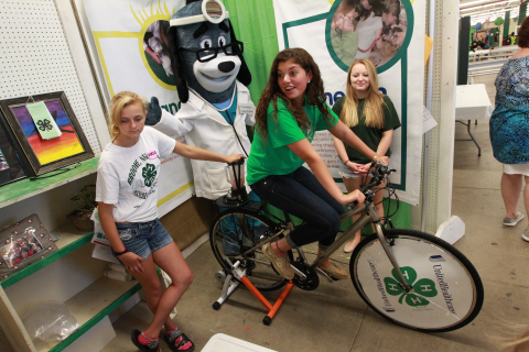 4-H Youth Health Ambassador Rose Rella of Central Valley, N.Y., creates her own smoothie using pedal power at the annual New York State Fair in Geddes, near Syracuse, on Aug. 21. The smoothie bikes are part of 4-H and UnitedHealthcare's partnership called "Eat4-Health," which helps tackle obesity by promoting healthy eating and lifestyles among youth and families. With her, from left, is Kristal Spencer, of Binghamton, UnitedHealthcare mascot Dr. Health E. Hound and April Turner of Central Valley (Photo: Michael J. Okoniewski for UnitedHealthcare).
