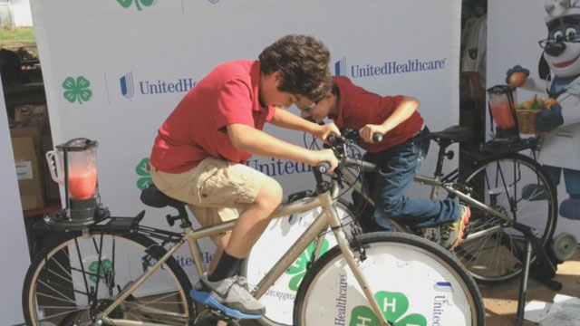 (L-R) Derek Molina (9) and Juan Maken (9) from Challenger Elementary School in Rio Rico are cheered on at the Santa Cruz County Fair in Sonoita by 4-H youth and fellow students, as they make their own healthy smoothies on new blender bikes donated to Arizona 4-H as part of a $40,000 grant from UnitedHealthcare (Video: Espe Greenwood).