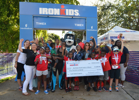 Candy Sicle, director, UnitedHealthcare of Florida, (front, wearing sunglasses) presents a $3,000 cheque to Tina Brown, executive director, Overtown Youth Center of Miami, (black and blue pants, 5th from left holding baby) to support the center's healthy living programs at today's UnitedHealthcare IRONKIDS Miami Fun Run at Bayfront Park. Photo Credit: Gaston De Cardenas