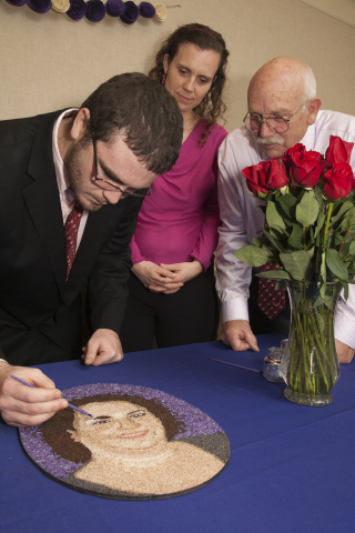Jay Zimmer adds bits of roasted coffee bean to the "floragraph" portrait of his mother, Heidi Zimmer, a SightLife cornea donor who will be honored on the DonateLife Rose Parade float on New Year's Day 2015. Heidi's sister, Lorilee Zimmer-Desantis (center), her father, Richard Zimmer (right) and other family and friends gathered recently to complete the floragraph created by float artisans. (Photo credit: SaraPress.com)