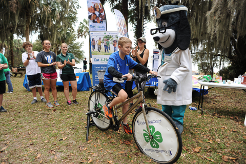 UnitedHealthcare’s mascot Dr. Health E. Hound cheers on Alachua County 4-H Members as they use a smoothie bike to create their own healthy snack in return for a little “sweat equity” at the annual “Little Run on the Prairie” 5K race at Payne’s Prairie Preserve State Park in Micanopy, FL. The smoothie-bike is part of $40,000 grant announced today from UnitedHealthcare to University of Florida’s Institute of Food and Agricultural Sciences (IFAS) that will promote healthy living among youth. (Photo credit: Julie Brewer Photography)