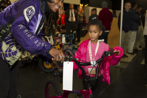 Volunteer from The Congregation Cycling Club helps a child with her new bicycle. (Photo: Business Wire)