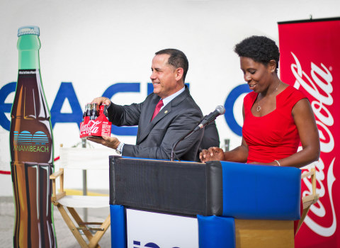 Melanie Jones, General Manager for Coca-Cola South Florida, present Miami Beach Mayor Philip Levine the first Miami Beach 100th Anniversary Commemorative Coca-Cola six-pack. (Photo: Business Wire)