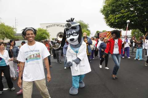 UnitedHealthcare mascot Dr. Health E. Hound leads a healthy walk across the East Point Bridge with the Common Ground Collective Jazz Band and community leaders, students, families and health care professionals to kick off a community health fair hosted by Morehouse, United Health Foundation, Optum and UnitedHealthcare at the Comprehensive Family Healthcare Center at Buggy Works in East Point. During the event, United Health Foundation and Optum announced a grant for $1.2 million to the Morehouse School of Medicine to support its Patient Centered Medical Home and Neighborhood Project. L to R: Makel Guice, freshman at Georgia State University; UnitedHealthcare mascot Dr. Health E. Hound; and Natosha Carroll, with the Common Ground Collective Jazz Band (Photo: Russell Kaye).