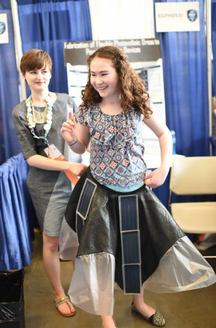 PITTSBURGH, Pa. May 14, 2015 - Allison Clausius, 18, of Toledo, Ohio, holds her cellphone charging dress at the waist of a young girl during the Intel International Science and Engineering Fair, the world's largest high school science competition. Approximately 1,700 high schoolers from 78 countries, regions and territories are competing for $4 million in awards this week. PHOTO CREDIT: Intel/Kathy Wolfe