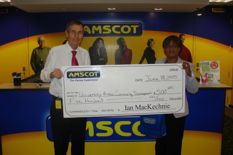 Ian MacKechnie Amscot CEO and founder, presents a check for $500, accepted on behalf of University Area Community Development Corporation, Inc. by Martine Dorvil, Director of Community Outreach. (Photo: Business Wire) 