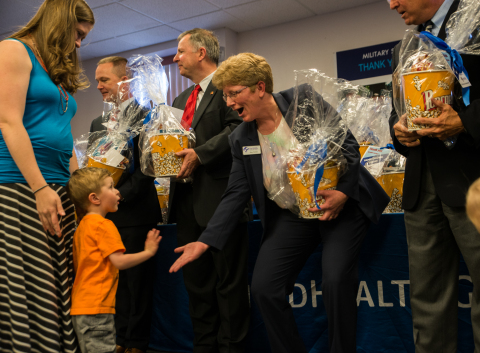 (L-R) Military spouse Lindsay Kester and son Elias, 3, receive a high-five from Kate Hatten, president and CEO, Peak Military Care Network, along with one of the 250 “Family Movie Night” gift baskets that were distributed as part of Military Spouse Appreciation Day in Colorado Springs, Colo. Also pictured l-r: Tom Wiffler, chief operating officer, UnitedHealthcare Military & Veterans, and U.S. Congressman Doug Lamborn (R-Colo.) (Photo: Teresa Lee).