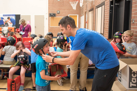 Six-year-old Cole Deyling receives a bike helmet from UnitedHealthcare Pro Cyclist Greg Henderson at a bike and helmet safety event at Hawthorne Elementary School in Boise, Idaho. UnitedHealthcare Pro Cyclists encouraged kids from the Boys & Girls club to be safe, stay active and participate in the upcoming Downtown Boise Twilight Criterium Kids’ ride event (Photo: Chad Case).