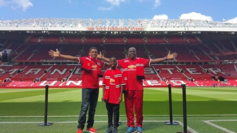 Taking It All In: “Here we are at Old Trafford – The Theatre of Dreams” one of two Flow Skills winners, 12 year Jamaican Brian Burkett (center) is flanked by his coach Mitchily Waul (left) and father, Albert Burkett (right). (Photo: Business Wire)