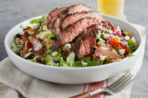 California Pizza Kitchen's delicious new Grilled Steak Salad features warm steak (cooked to medium) served over chopped lettuce & arugula, Nueske’s® applewood smoked bacon, jicama, red cabbage, charred red onion petals, tomatoes and Gorgonzola, tossed in bleu cheese dressing. (Image courtesy of California Pizza Kitchen)