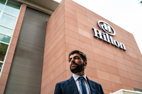 Hilton Team Member Ismaeil Dawod stands in front of the Hilton Frankfurt where he participates in an apprenticeship program that gives him exposure to various hotel departments. (Photo: Hilton)