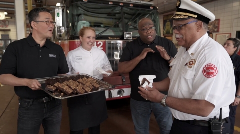 Team Members from The Palmer House, a Hilton Hotel, surprised the firefighters of River North’s Engine Co. 42 Fire House with a Random Act of Hospitality in celebration of Hilton’s 100th anniversary. Led by hotel manager Detraiter Love, second from right, Team Members thanked the Chicago Fire Department by treating firefighters to a brownie – a sweet treat that originated at The Palmer House during the Chicago World’s Fair.  (Credit: Hilton)