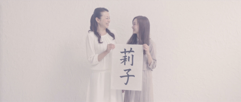 A mother and daughter smile at each other as they hold up the paper with the daughter’s name written in calligraphy. Viewers can tell from their expressions as they look at each other that they understood each other’s feelings through the video letter. (Photo: Business Wire)