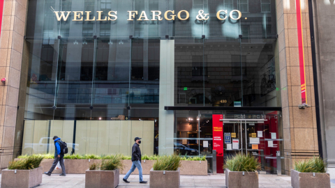 External view of Wells Fargo building with a glass front and individuals walking by on sidewalk. (Photo: Business Wire)