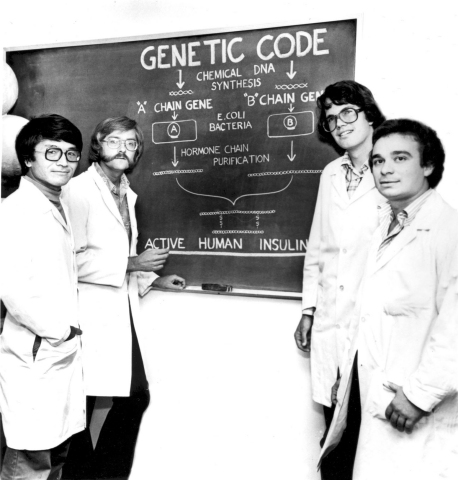 Keiichi Itakura, Ph.D., far left, and Arthur Riggs, Ph.D., left, with a chart explaining how they used the genetic code of E. coli bacteria to manufacture synthetic human insulin. Photo Credit: City of Hope