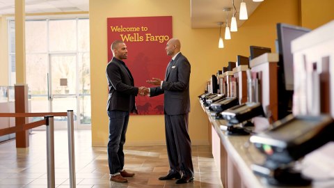 Male Wells Fargo employee shaking hands with another male in front of a teller line. (Photo: Wells Fargo)