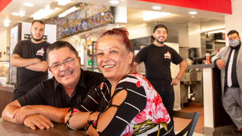 Male and female small business owners sitting side by side with three staff members standing in the background. (Photo: Wells Fargo)