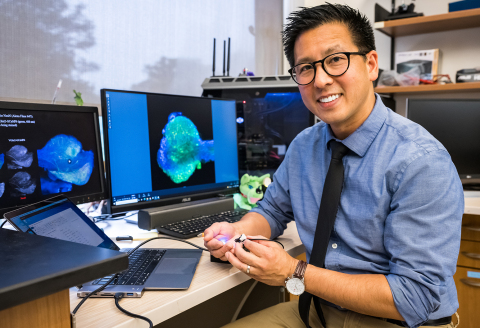 original Eric H. Chang, assistant professor in the Institute of Bioelectronic Medicine at the Feinstein Institutes holds up a miniature epi-fluorescence microscope. (Credit: The Feinstein Institutes for Medical Research)