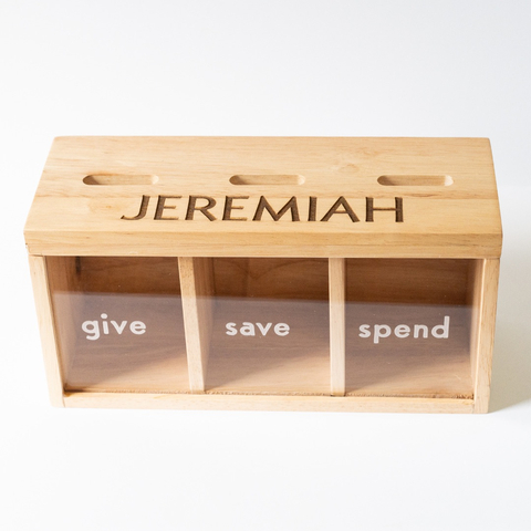 original The new design for the Enduring Legacy Bank launched in October 2022. Each piggy bank can be personalized with a child's name engraved as seen here. In addition, parents can choose from a variety of front panel categories such as GIVE, TITHE, or TZEDAKAH. Each bank is fully customizable with 3 wood finishes and 3 font options to choose from. (Photo: Business Wire)