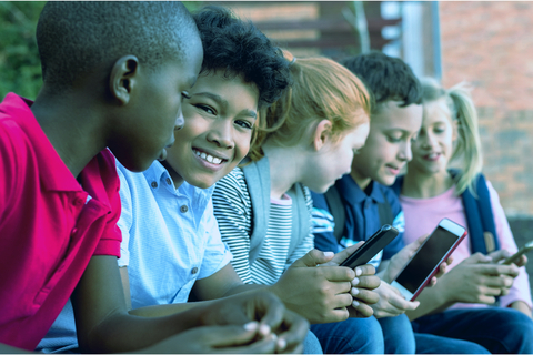 Five seated children smiling and looking at smartphones (Photo: Business Wire)