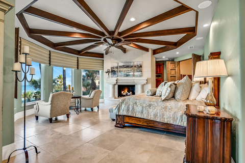 In the primary bedroom suite, a wall of windows offers direct ocean views, while features like exposed wood beams and a stone fireplace add depth and character to the interiors. OceanfrontLuxuryAuction.com. (Photo: Business Wire)