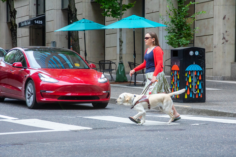 A woman and her guide dog cross a busy street. (Photo: Business Wire)