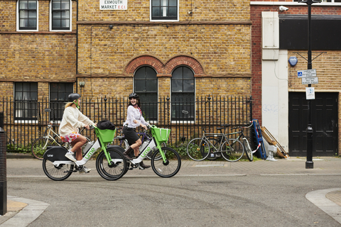 Two young women ride Lime electric bikes through a city. (Photo: Business Wire)