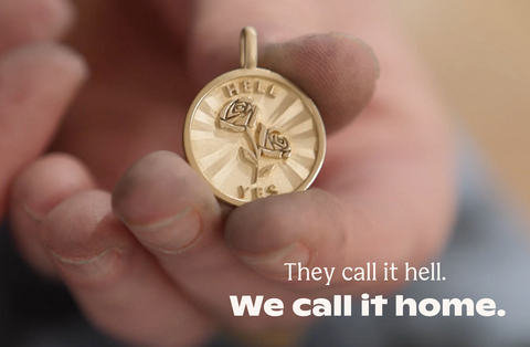 A maker's hands holds Betsy & Iya's Hell Yes medallion in their Portland, OR production studio.