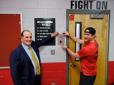 Anthem Blue Cross and Blue Shield of GA, RVP, Rob Teas, and Founder and President of Impact Fitness Foundation, Chris Walsh, hang a plaque on the wall of the new weight room.