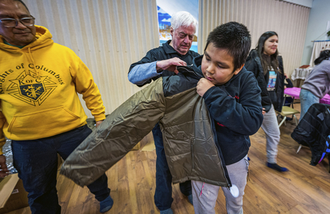 Le 26 février 2026, Cleo Castillo et Vaughn Wadelius, membres des Chevaliers de Colomb, aident un garçon à enfiler un nouveau manteau au sein de la communauté isolée des Premières Nations de Pukatawagan, dans le nord du Manitoba. Les Chevaliers ont livré 22 lits, ainsi que 500 manteaux et 10 fauteuils roulants à la communauté, à la suite d’un long voyage depuis Winnipeg sur des routes enneigées. (Photo de Colby Spence)