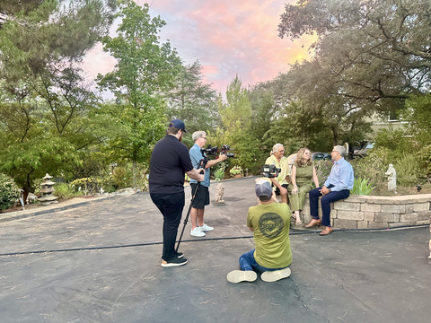 Filming a scene of Senior Spaces are Berkshire Hathaway HomeServices California Properties' agent Bryan Devore (sitting right), along with Rick and Mary Williams (also sitting, the stars), Ryan Niesz (in blue, the producer), Mark Eidbo (in black, camera person), and Aaron Lawler (kneeling, camera person).