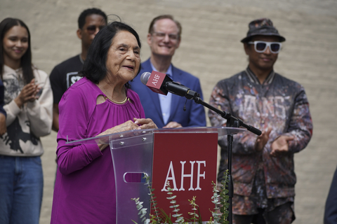 original Dolores Huerta, American labor leader and civil rights activist who co-founded the United Farm Workers Union, addresses the crowd at the dedication of a new mural by artist Robert Vargas honoring her at a ceremony hosted by AHF on Saturday, May 16, 2026, in Downtown Los Angeles, California. To her right is AHF President Michael Weinstein and muralist Robert Vargas (far R) . The mural, titled “Walking into History,” is on a six-story wall of the historic Barclay Hotel, the oldest continually operating hotel in Los Angeles and one of Housing4Humanity’s affordable housing hotels housing formerly homeless and extremely low-income individuals. This was Huerta’s first community appearance since her recent groundbreaking disclosures to the New York Times.