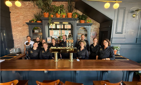original Staff of Grouchy’s Pub celebrating their opening, including owner Breck Nelson (third from right), his daughter Rosie (second from right, owner of the bookstore), and his wife Janie Nelson, owner of the coffee shop and plant store.