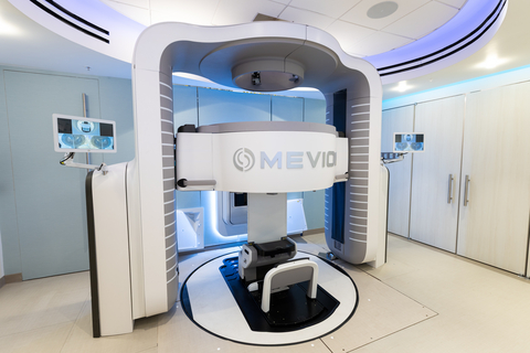 original The treatment room at Stanford Medicine Cancer Center, Palo Alto, California, housing the Marie® upright patient positioning platform by Leo Cancer Care (center foreground) integrated with the Mevion S250-FIT™ Proton Therapy System. The circular rotating platform enables a patient seated in the Marie® chair to rotate 360 degrees in relation to a fixed proton beam — replacing the large rotating gantries required by traditional proton therapy systems. This compact configuration, which requires approximately 1,700 square feet compared with over 29,000 square feet for conventional proton therapy facilities, was used on June 4, 2026 to complete the world's first compact upright proton therapy patient treatment. The Marie® system is powered by RayStation from RaySearch. Photo: Steve Fisch / Stanford Medicine