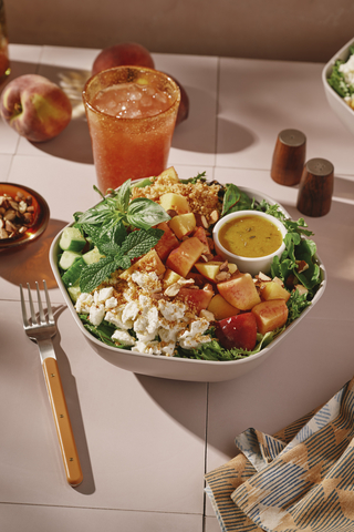 thumbnail The salad is made with organic arugula and spring mix, peaches, goat cheese, cucumbers, basil, mint and almonds, then finished with lemon tarragon vinaigrette and garlic parm crunch.