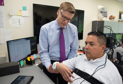 original Dr. Chad Bouton of Northwell Health’s Feinstein Institutes for Medical Research assists setting up Keith Thomas with a non-invasive wearable stimulation patch worn over the skin, part of the “double neural bypass” clinical trial.
