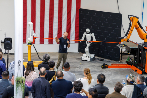 A humanoid robot cuts the ribbon at Formic's Oakland facility grand opening on August 19, 2026, flanked by an industrial robot arm, as attendees look on.