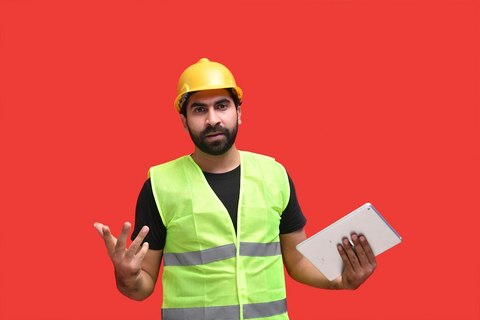 A construction worker in a safety vest holding and reviewing a tablet on a job site.
